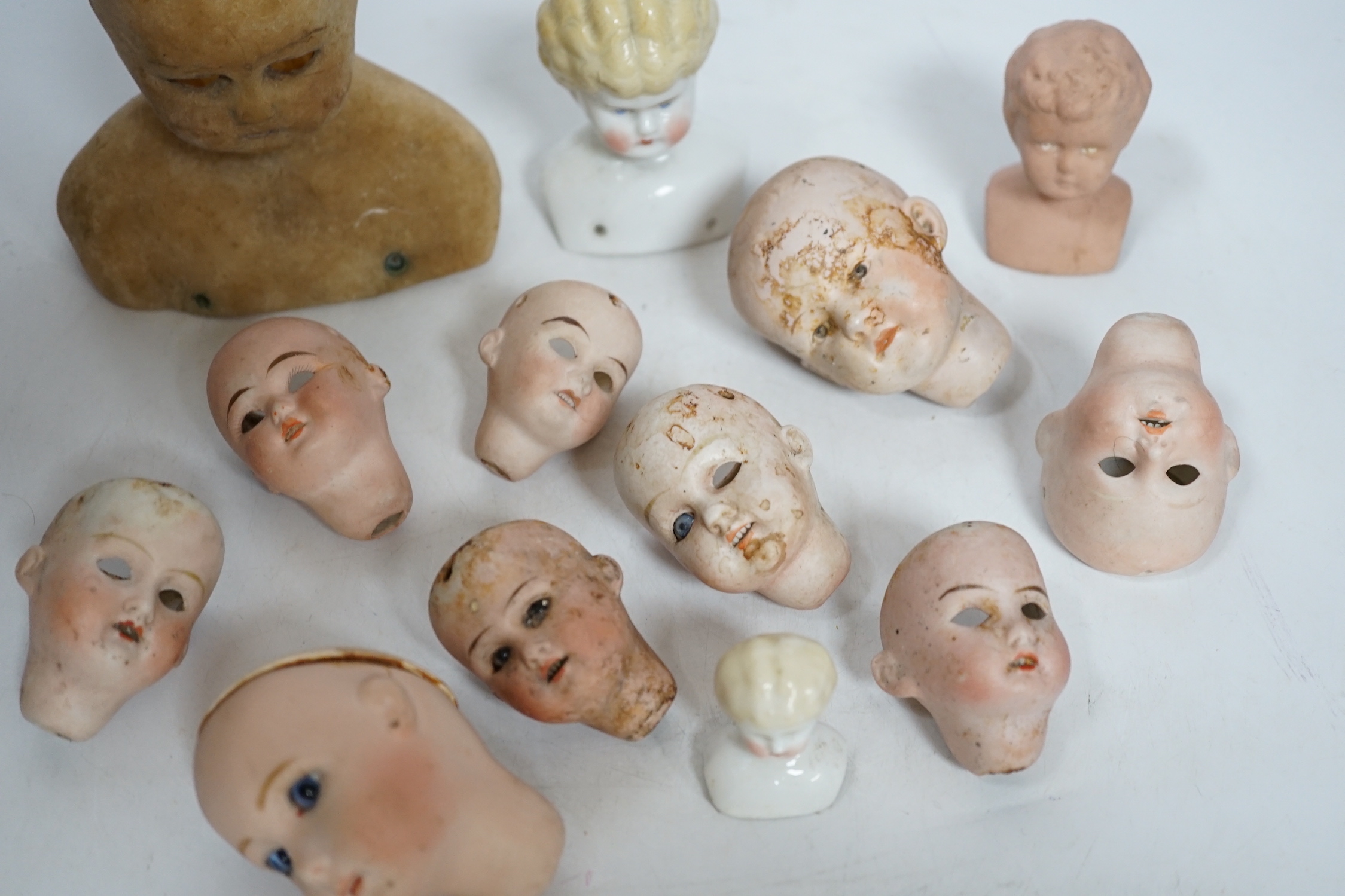 Twelve small bisque doll heads and a wax head